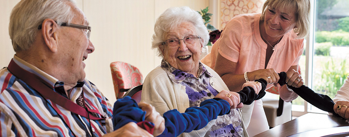 Op de foto ziet u twee bejaarde mensen met dementie samen met een activiteitenbegeleider spelen met de co-operband van SpelPlus een winkel speciaal voor spelletjes voor ouderen. Ze hebben veel plezier met deze activiteit voor dementerenden.